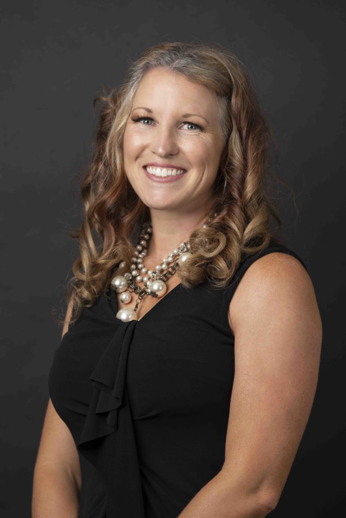 Professional headshot of businesswoman in black dress with statement necklace